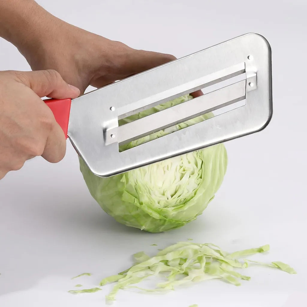 Hand using red-handled stainless steel cabbage shredder to slice green cabbage on white background