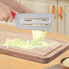 Red-handled cabbage slicer shredding green cabbage onto wooden cutting board in kitchen setting